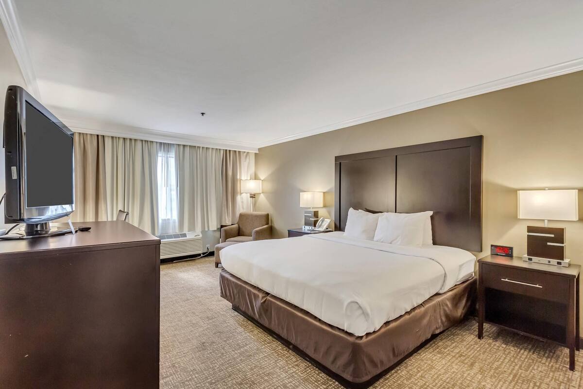 A hotel room with a large bed, a TV, a desk, and a nightstand with a clock.