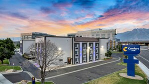 A modern hotel with a sign for Comfort Inn, surrounded by a parking lot and a mountain range in the background. - Comfort Inn Murray - Salt Lake City South (Murray)