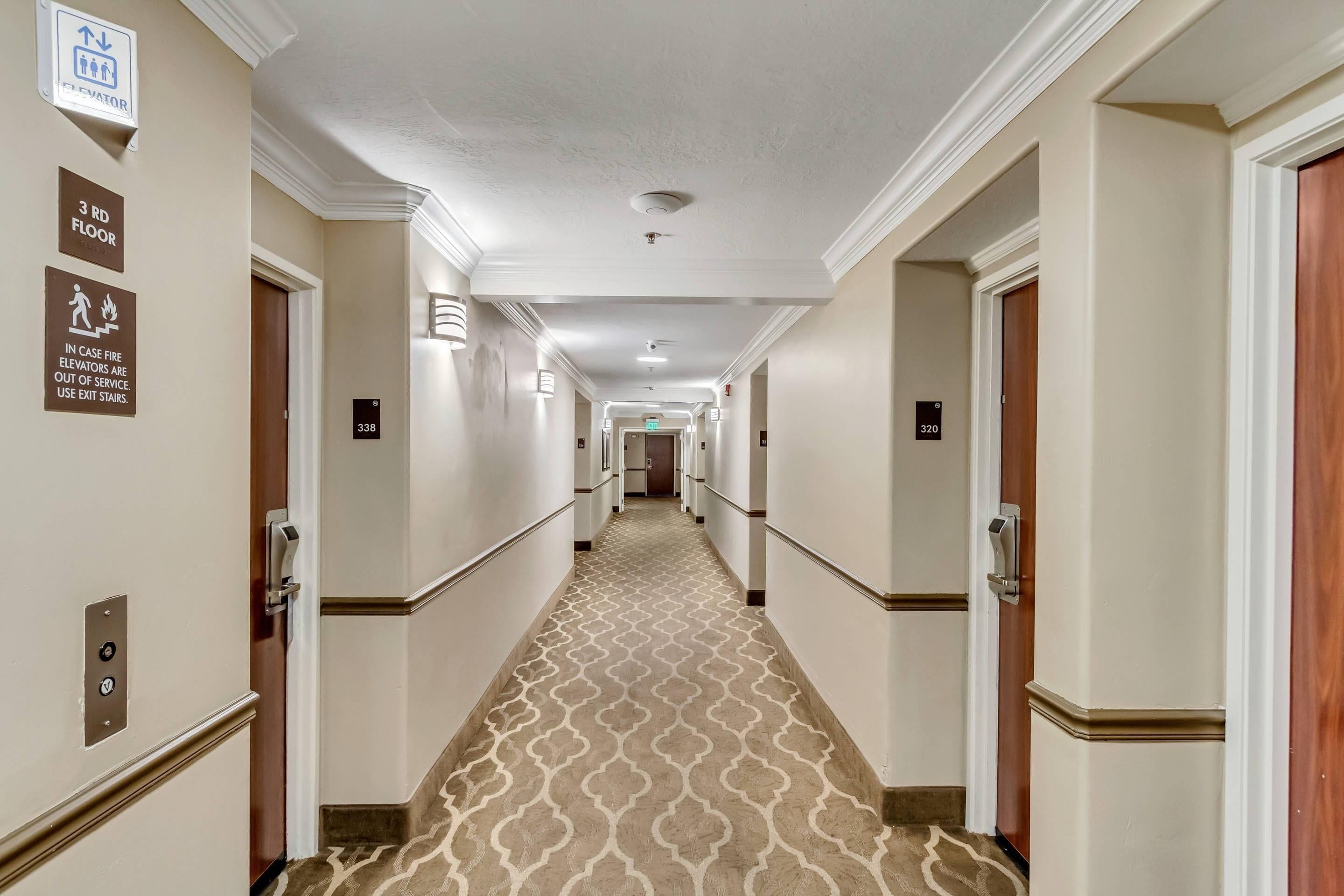 Ein Hotelgang mit einem gemusterten Teppich, weißen Wänden und den nummerierten Türen 338 und 320.