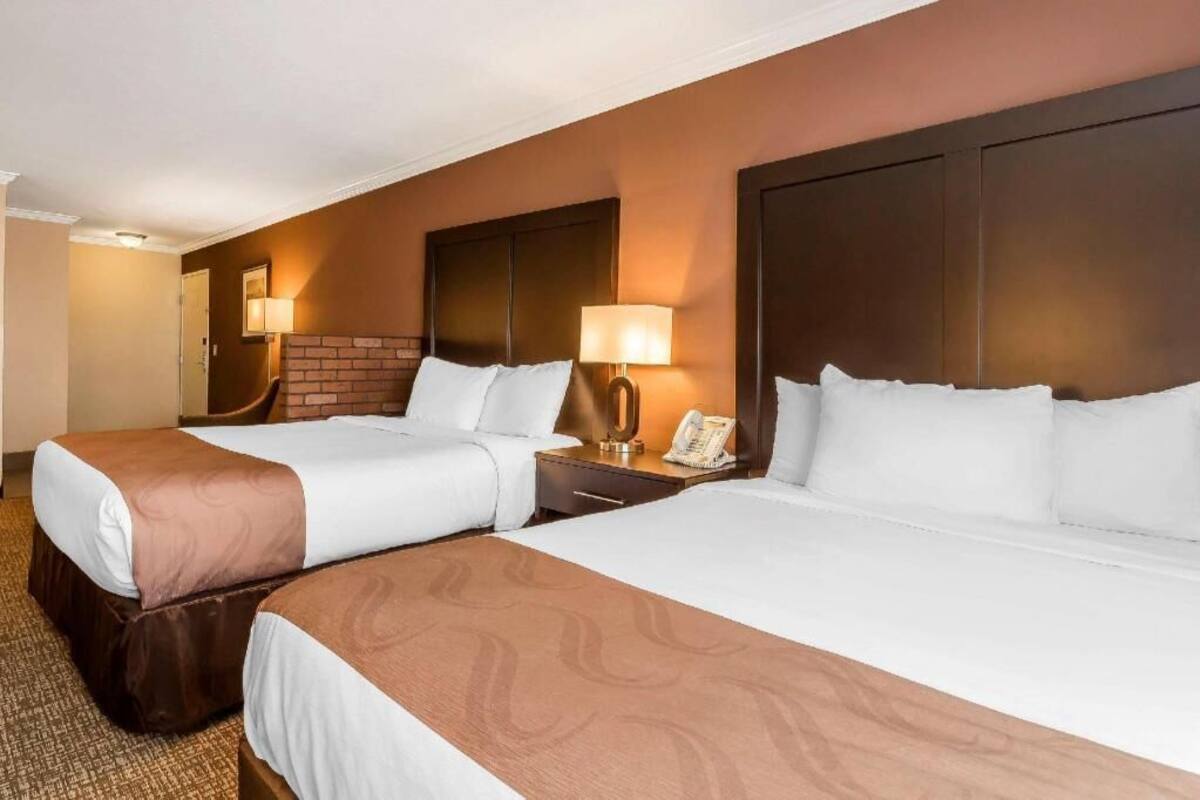 A hotel room with two beds, a brick fireplace, bedside lamps, and a telephone on the nightstand.