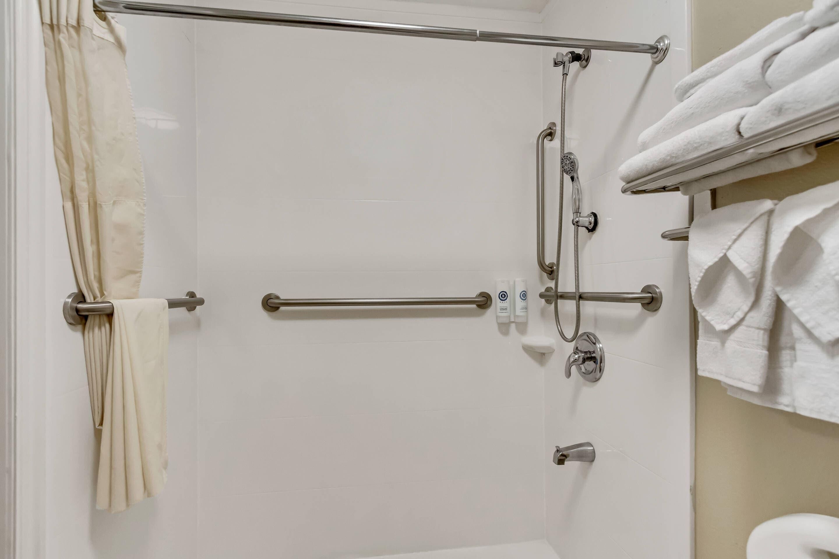 Une salle de bain avec une douche à parois de verre, des barres d’appui, un porte-serviettes et des toilettes.