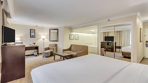 A hotel room with a large bed, a desk with a computer, a chair, a sofa, a TV, and a bathroom visible through a glass door. - Comfort Inn Murray - Salt Lake City South (Murray)