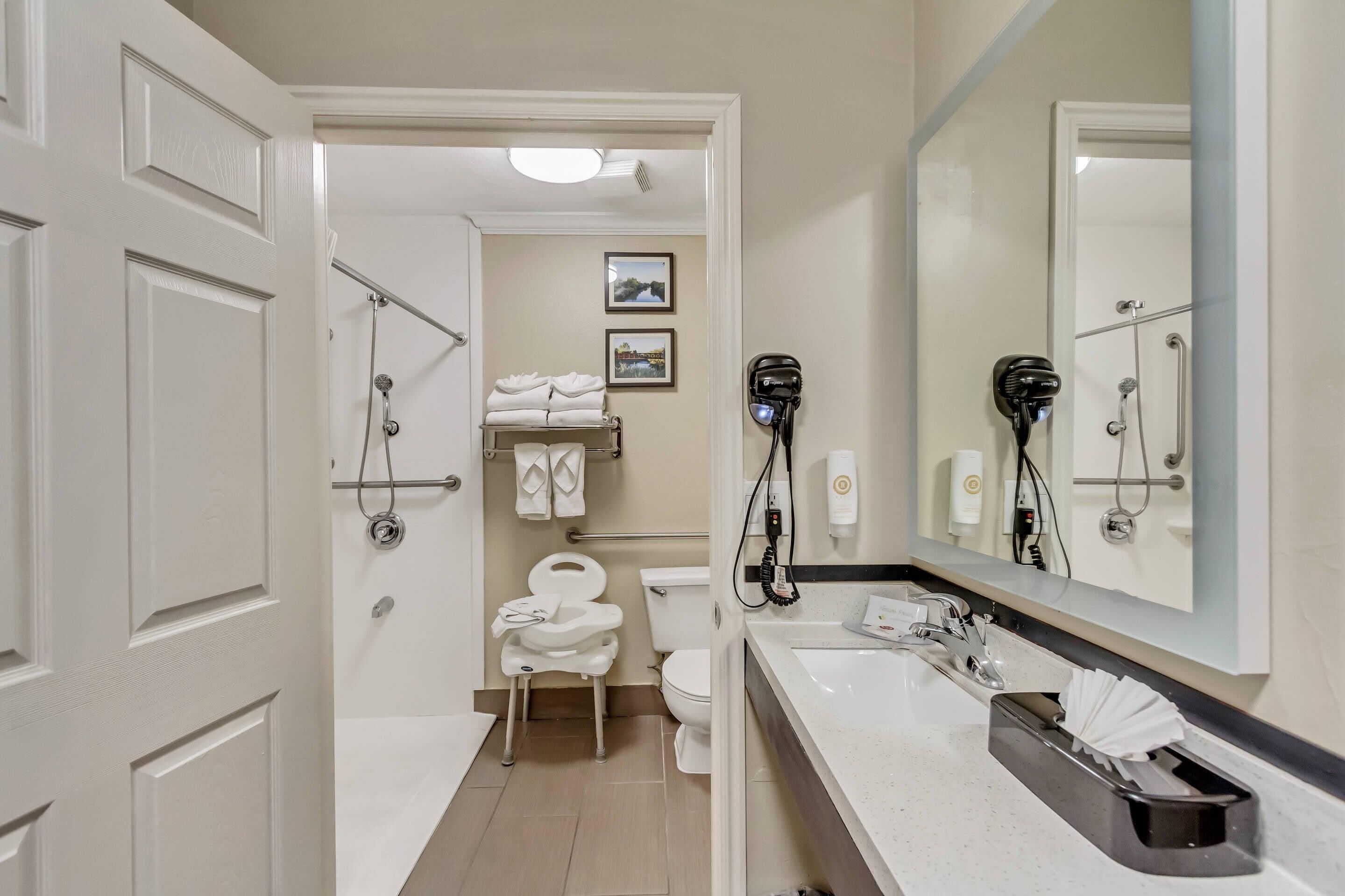 Une salle de bain moderne équipée d’une douche, de toilettes et d’un lavabo. Des serviettes et un sèche-cheveux sont accrochés au mur.