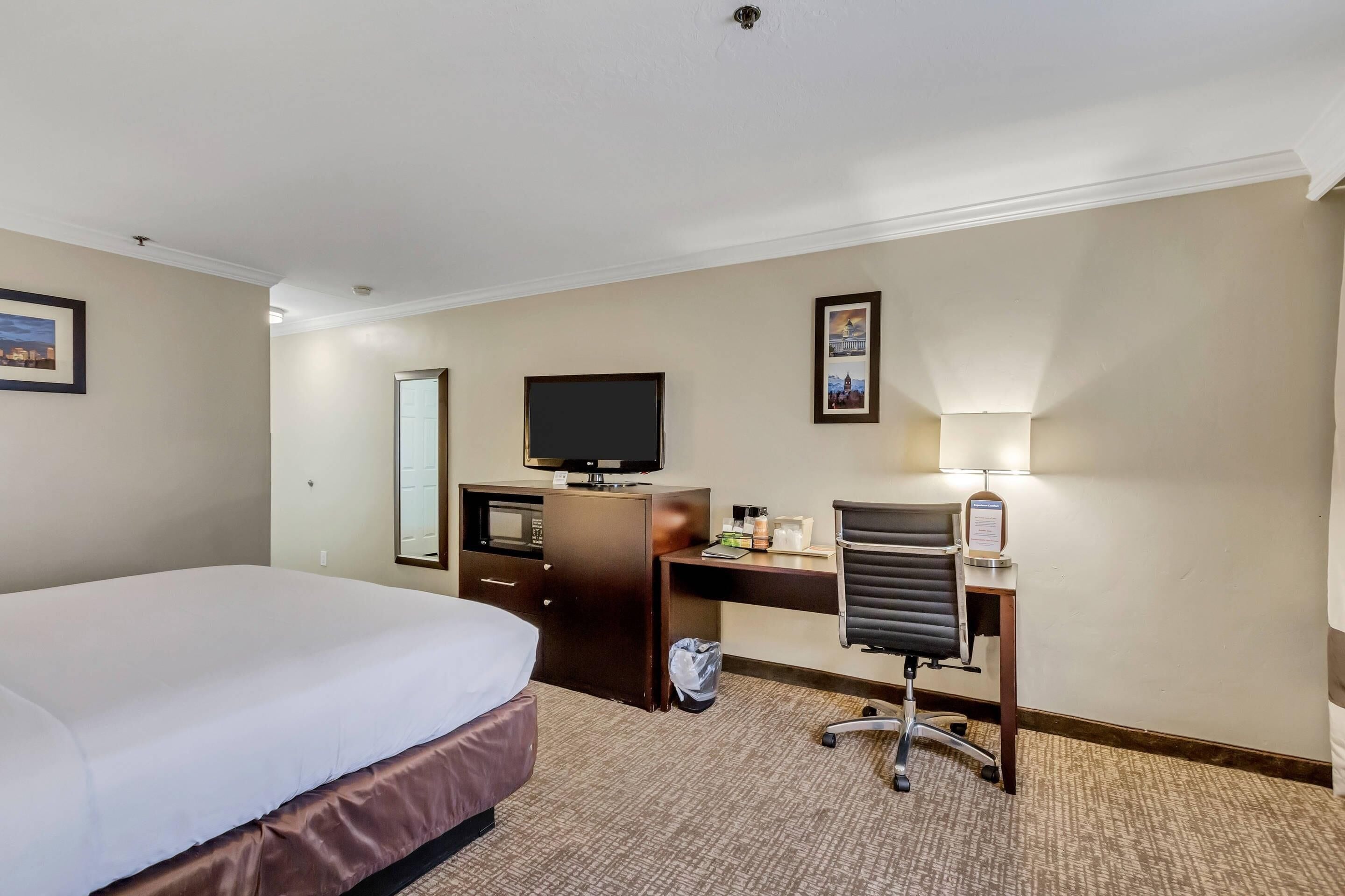 Una habitación de hotel con cama, escritorio, silla, televisor y lámpara.