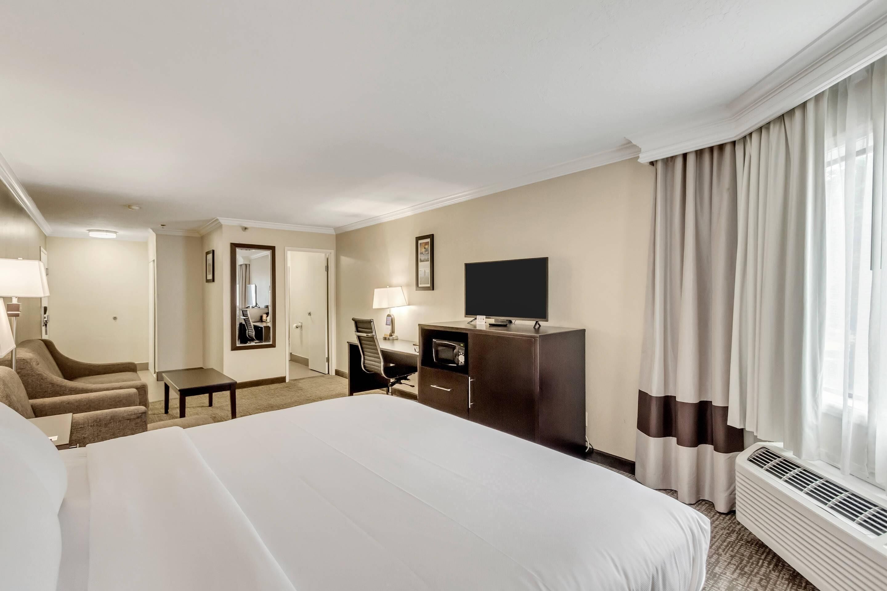 Une chambre d’hôtel avec un grand lit, un bureau avec une chaise, une télévision et une fenêtre avec des rideaux.
