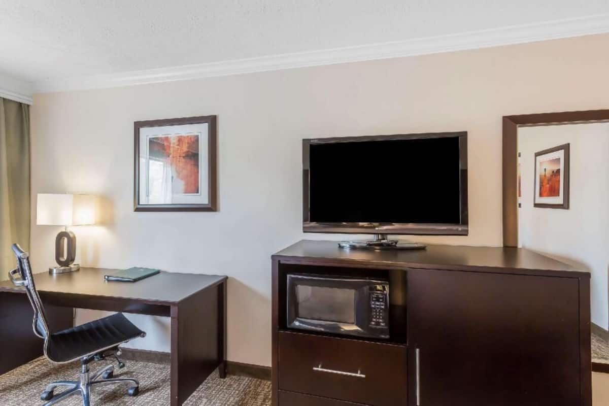 A hotel room with a desk, chair, television, microwave, and framed artwork on the walls.