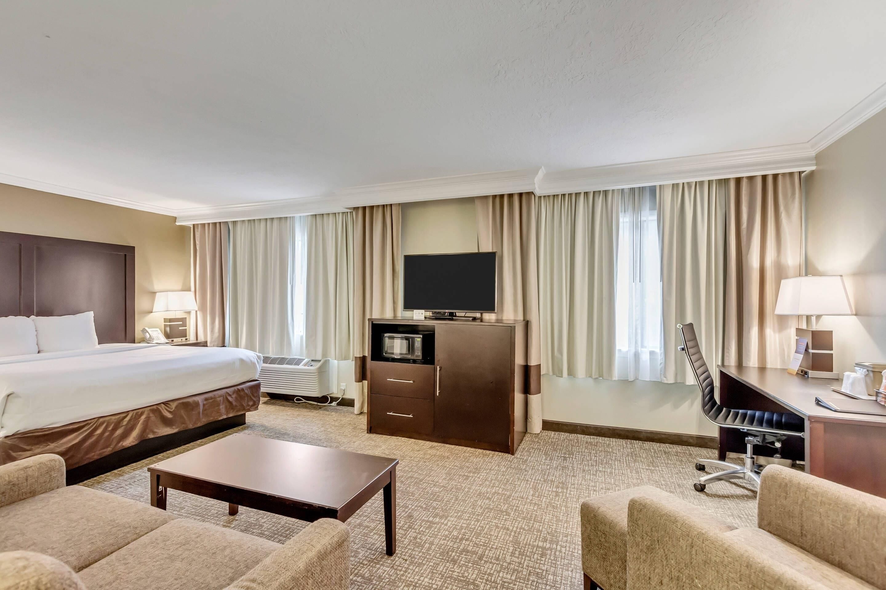 A hotel room with a bed, a desk with a chair, a television, and a minibar.