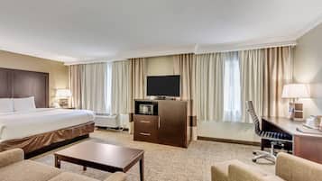 A hotel room with a bed, a desk with a chair, a television, and a minibar.