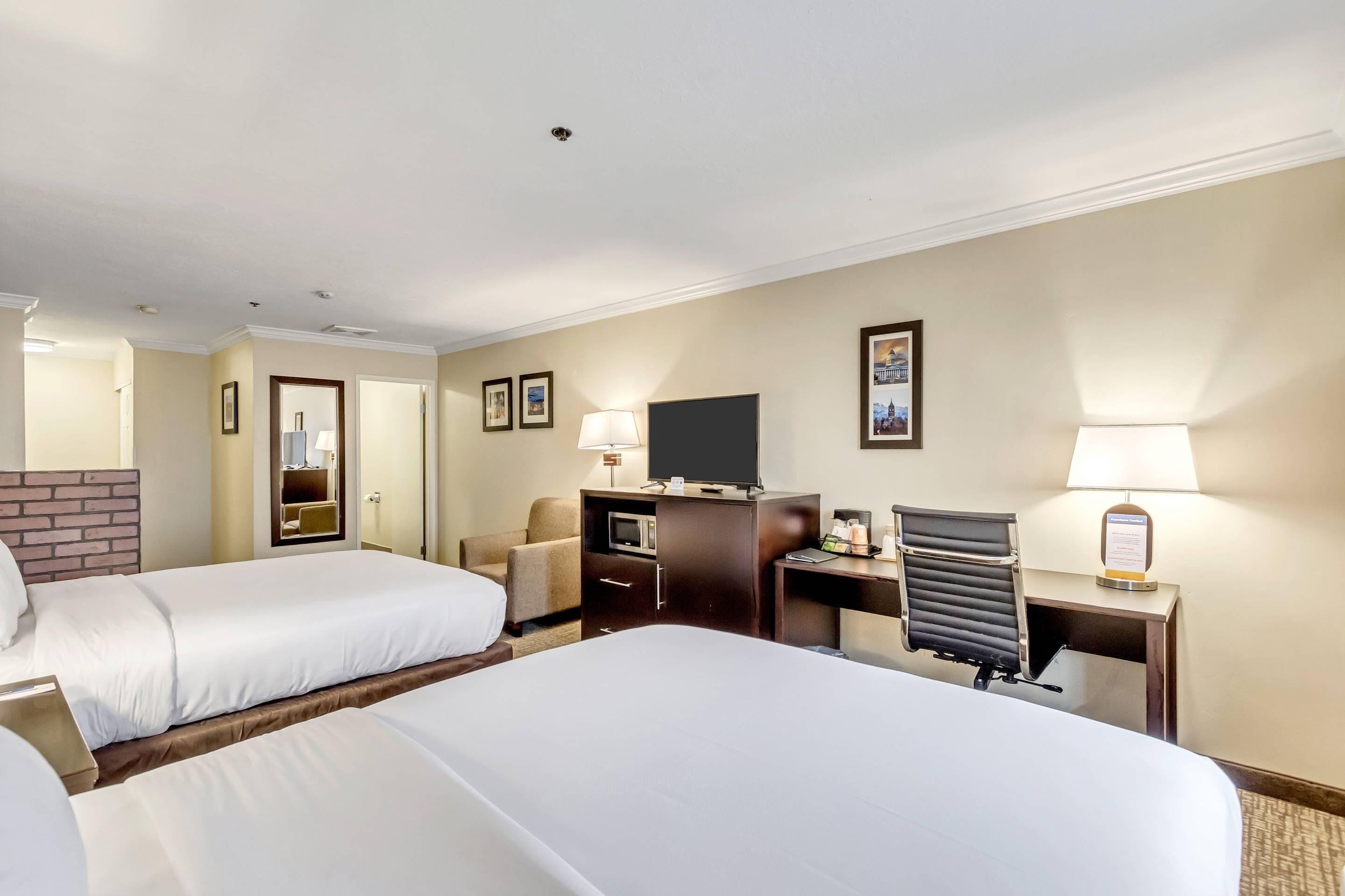 A hotel room with two beds, a desk, a chair, a television, and a lamp.