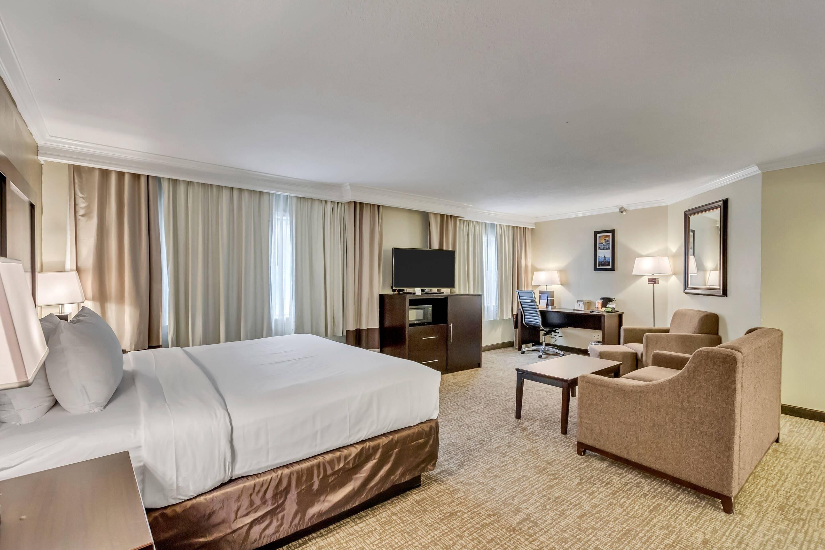 Una habitación de hotel con una cama grande, un escritorio con una computadora, un televisor y una zona de estar con sillas.