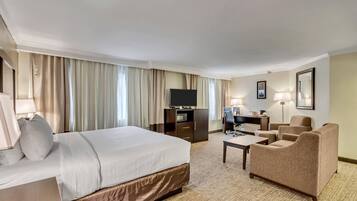 Una habitación de hotel con una cama grande, un escritorio con una computadora, un televisor y una zona de estar con sillas.