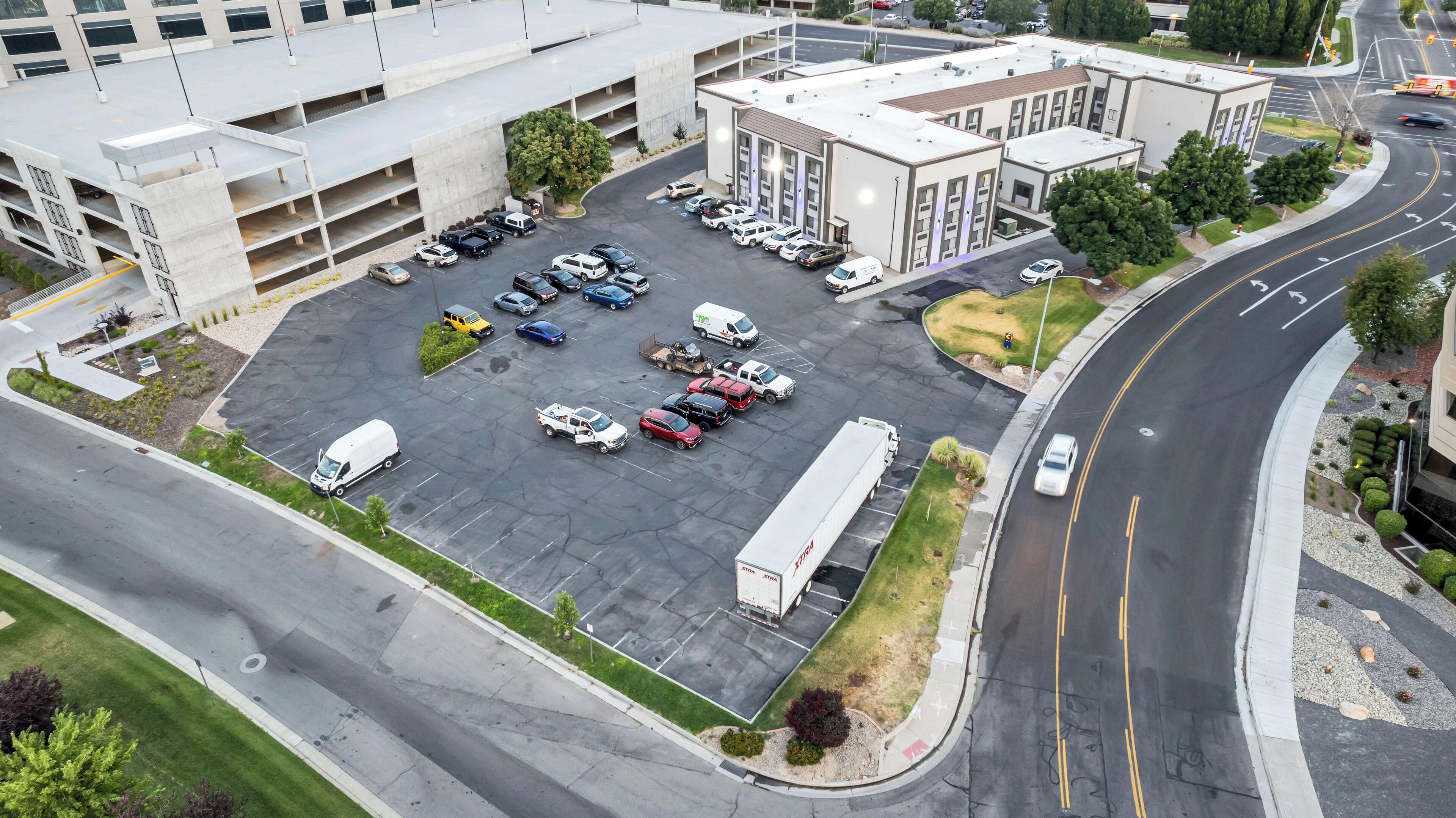An aerial view of a parking lot with multiple vehicles, including cars and trucks, and a building with a flat roof and large windows.