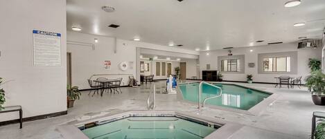 Una piscina interior con múltiples carriles, un letrero de precaución en la pared y una zona de estar con mesas y sillas.