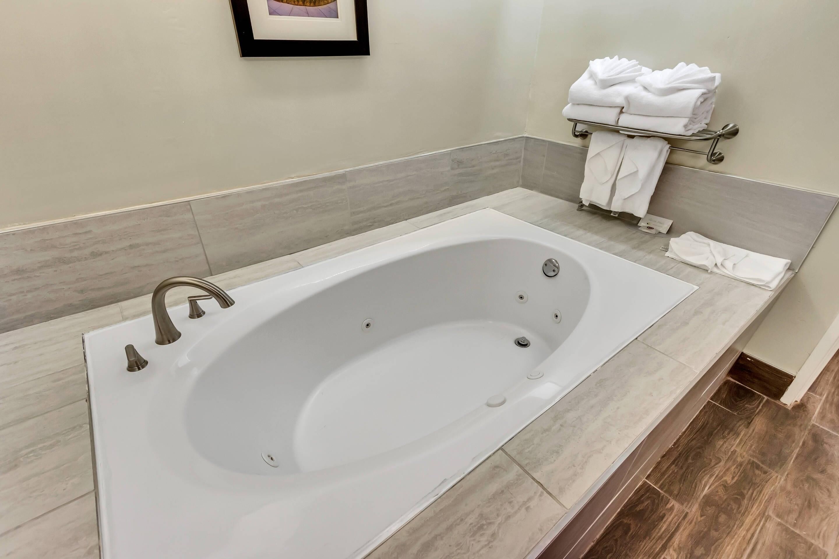 Un baño moderno con una bañera grande, un perchero con toallas dobladas y un cuadro en la pared.