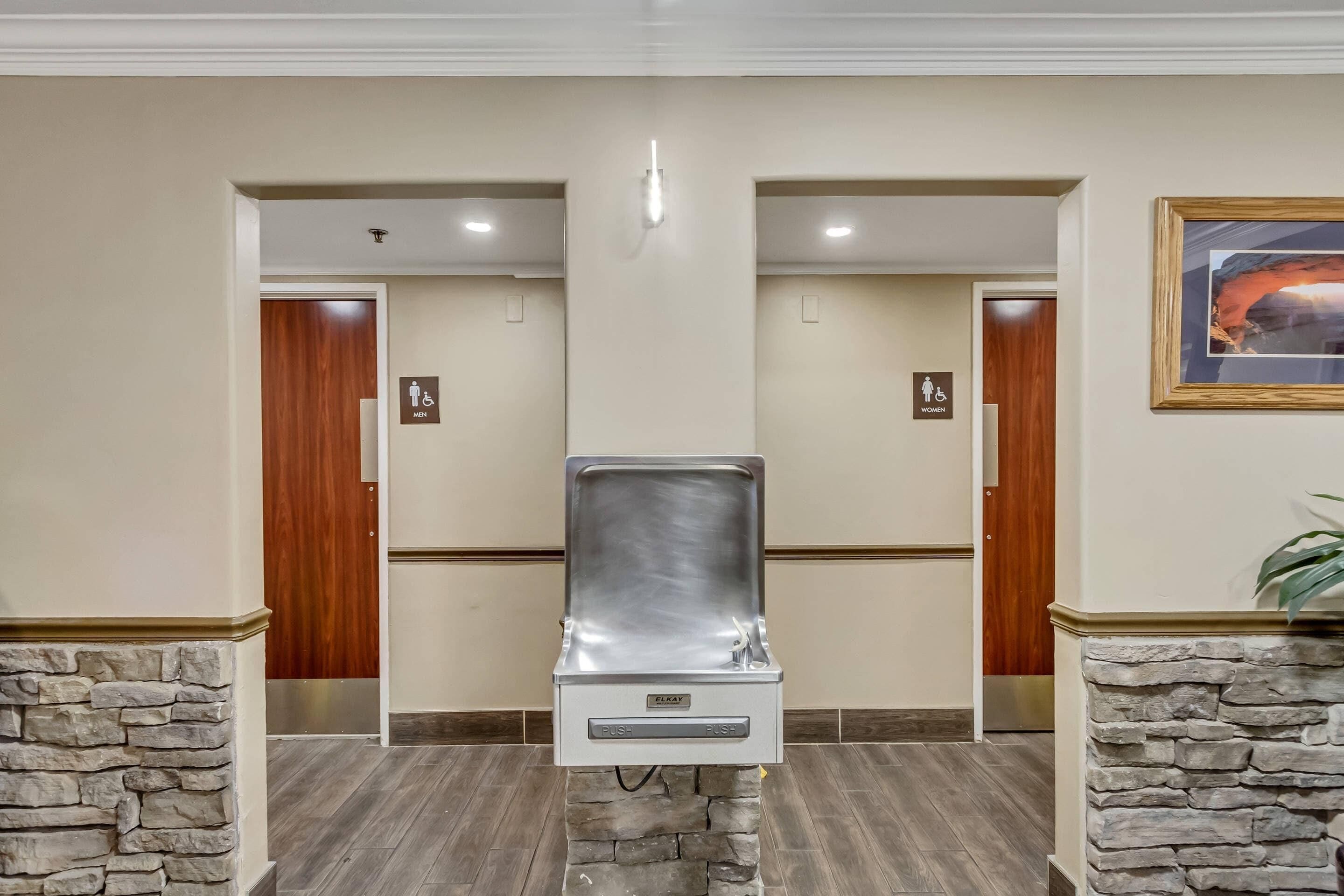 A restroom with a stainless steel sink, wooden doors, and a stone accent wall.