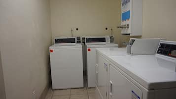 A laundry room with three stacked washers and dryers, a sign for bleach and softeners, and electrical outlets on the wall.