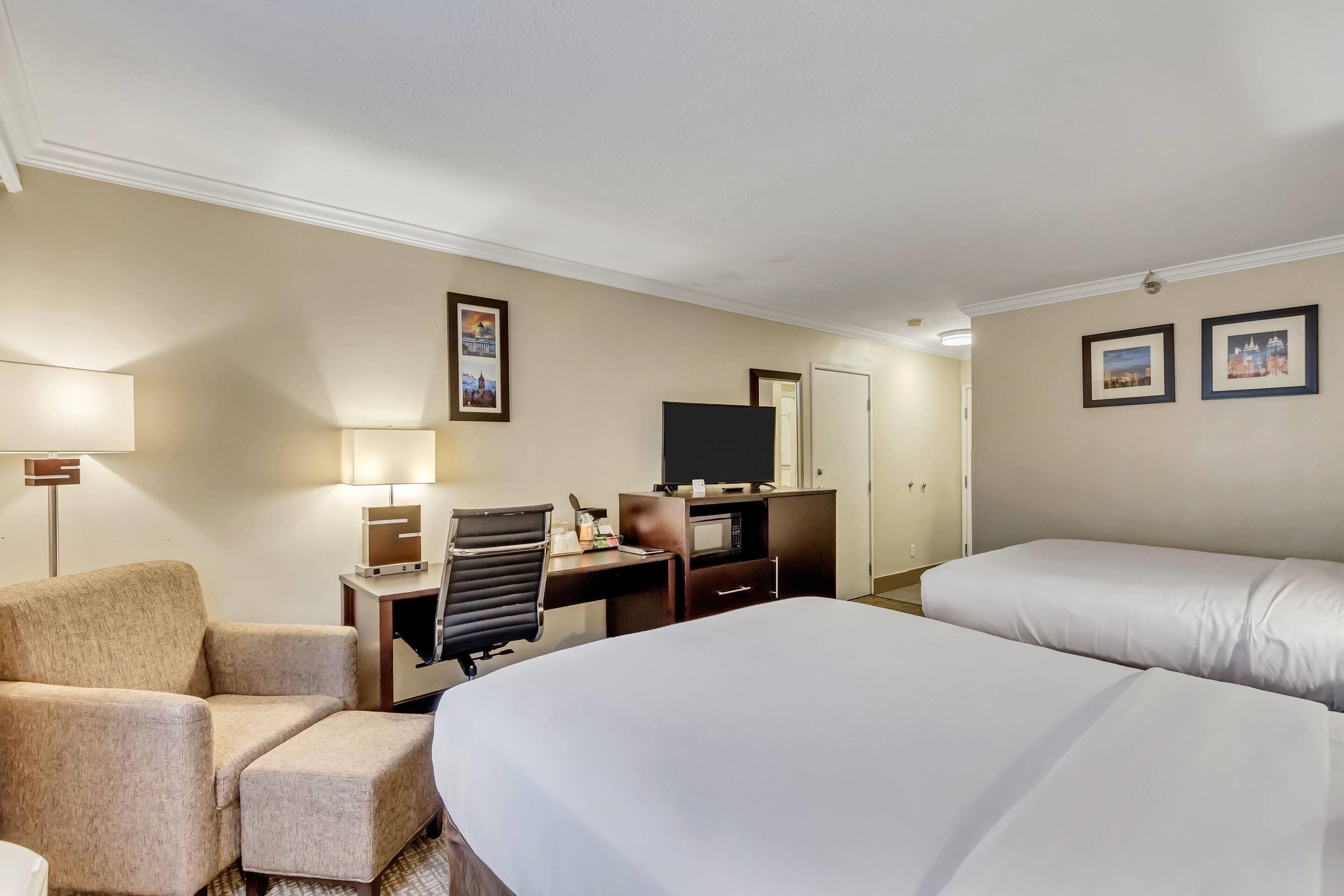 Una habitación de hotel con una cama, un escritorio con una silla, un televisor y una lámpara.