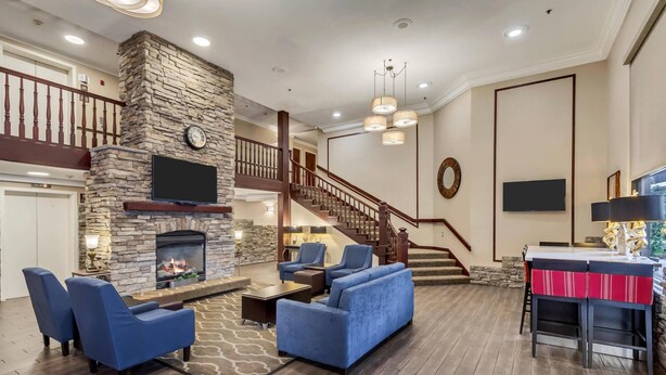 A spacious living area with a stone fireplace, blue sofas, a staircase, and a bar area. - Comfort Inn Murray - Salt Lake City South (Murray)