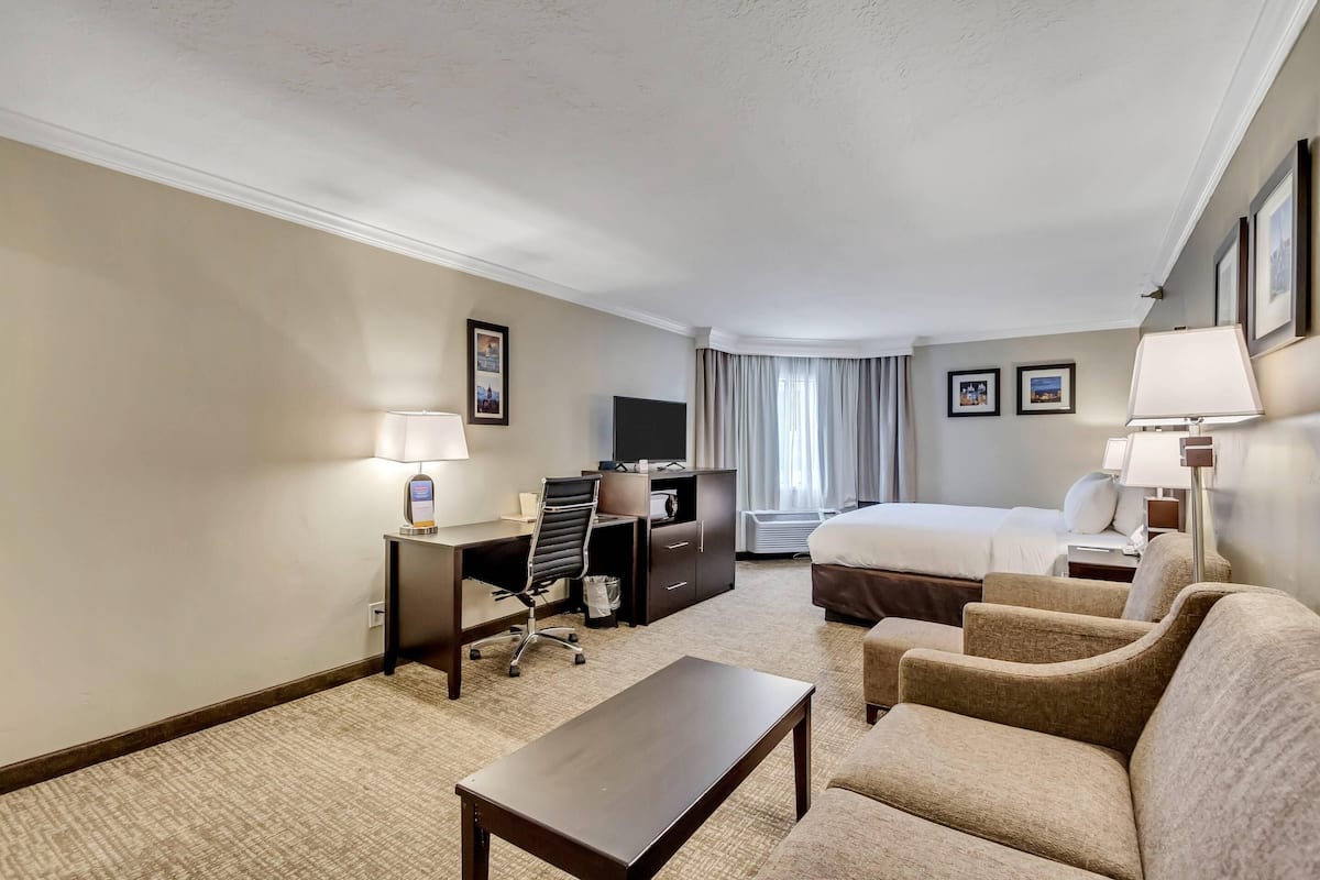 A hotel room with a bed, a desk with a chair, a sofa, and a television.