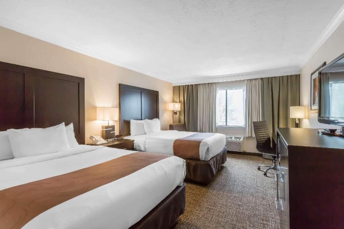 A hotel room with two beds, a desk, a chair, a TV, and a window with curtains.