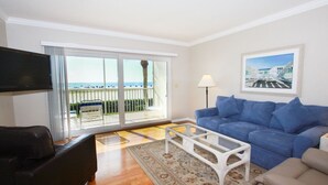 A living room with a blue sofa, a coffee table, a TV, and a balcony with a view of the sea. - Gulfview Manor Resort (Fort Myers Beach)