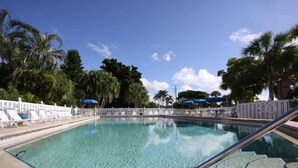 A clear swimming pool with lounge chairs and umbrellas, surrounded by palm trees and a clear sky. - Gulfview Manor Resort (Fort Myers Beach)