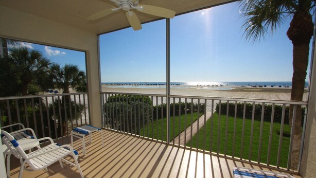 A balcony with a view of the beach and ocean, a ceiling fan, and a small table with chairs. - Gulfview Manor Resort (Fort Myers Beach)