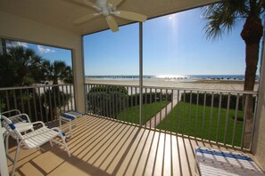 Un balcon avec vue sur la plage et l’océan, un ventilateur de plafond et une petite table avec des chaises.