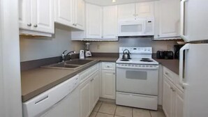 A compact kitchen with white cabinets, a microwave, a stove, and a dishwasher. - Gulfview Manor Resort (Fort Myers Beach)