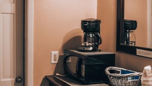 A kitchenette with a coffee maker, microwave, basket, and stacked cups. - Cottages on the Green (Pensacola)