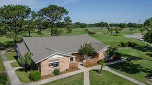 A two-story brick house with a sloped roof, a front porch, and a well-maintained lawn. - Cottages on the Green (Pensacola)
