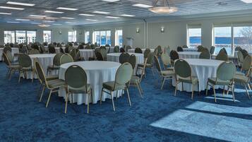 Une grande salle de conférence dotée de tables rondes et de chaises, de grandes fenêtres offrant une vue sur l’eau et d’un sol recouvert d’une moquette bleue.