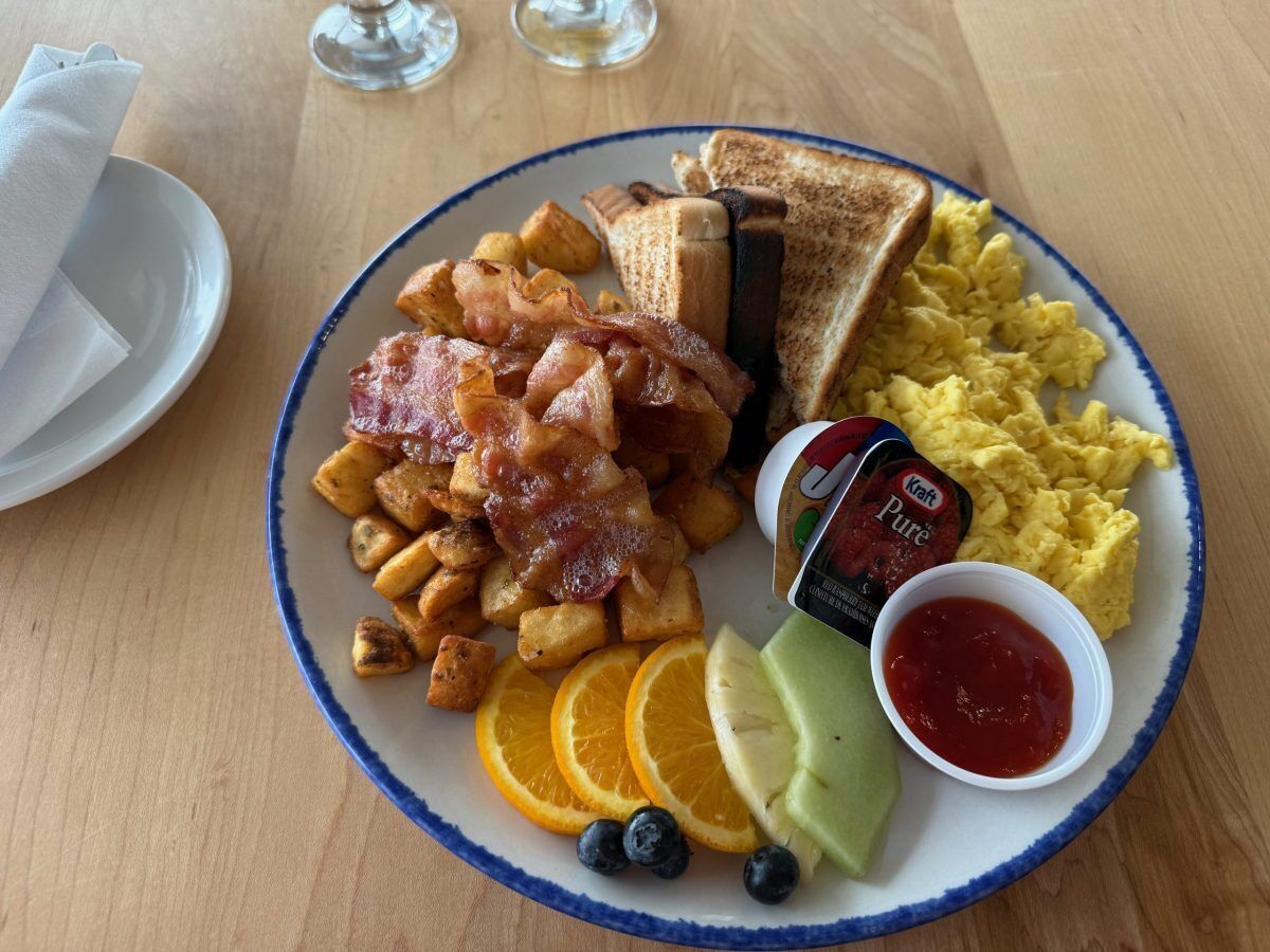 Un plato de desayuno con tostadas, huevos revueltos, tocino, patatas ralladas y fruta.