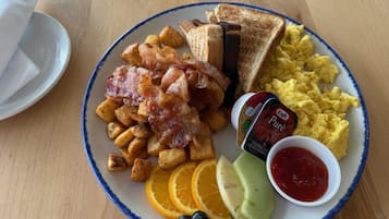 Un plato de desayuno con tostadas, huevos revueltos, tocino, patatas ralladas y fruta.
