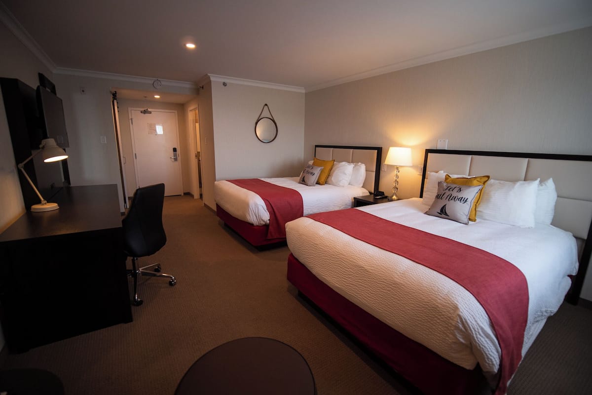 A hotel room with two beds, a desk, a chair, and a round table.