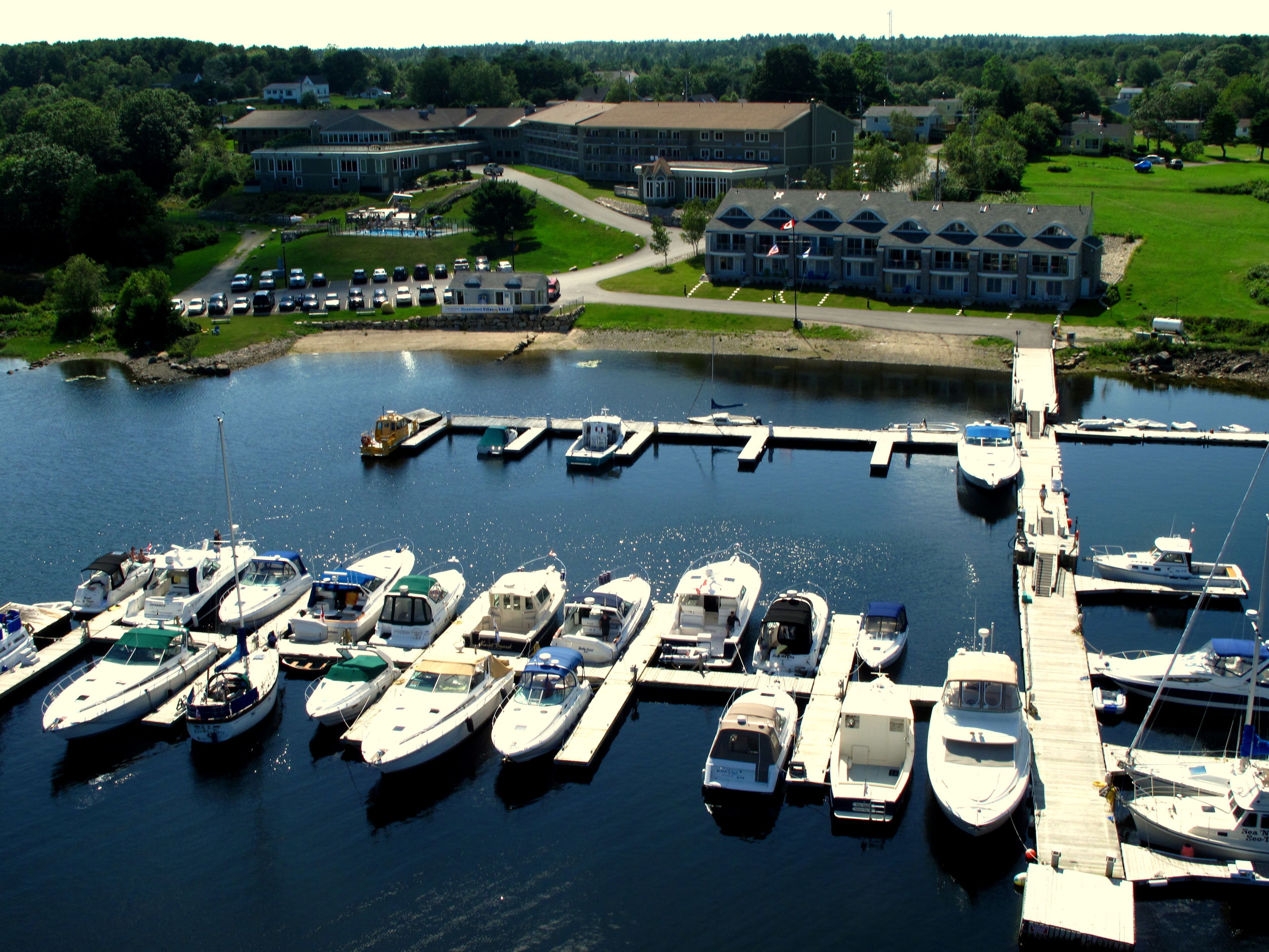 A marina with various boats docked, a dock extending into the water, and buildings in the background.