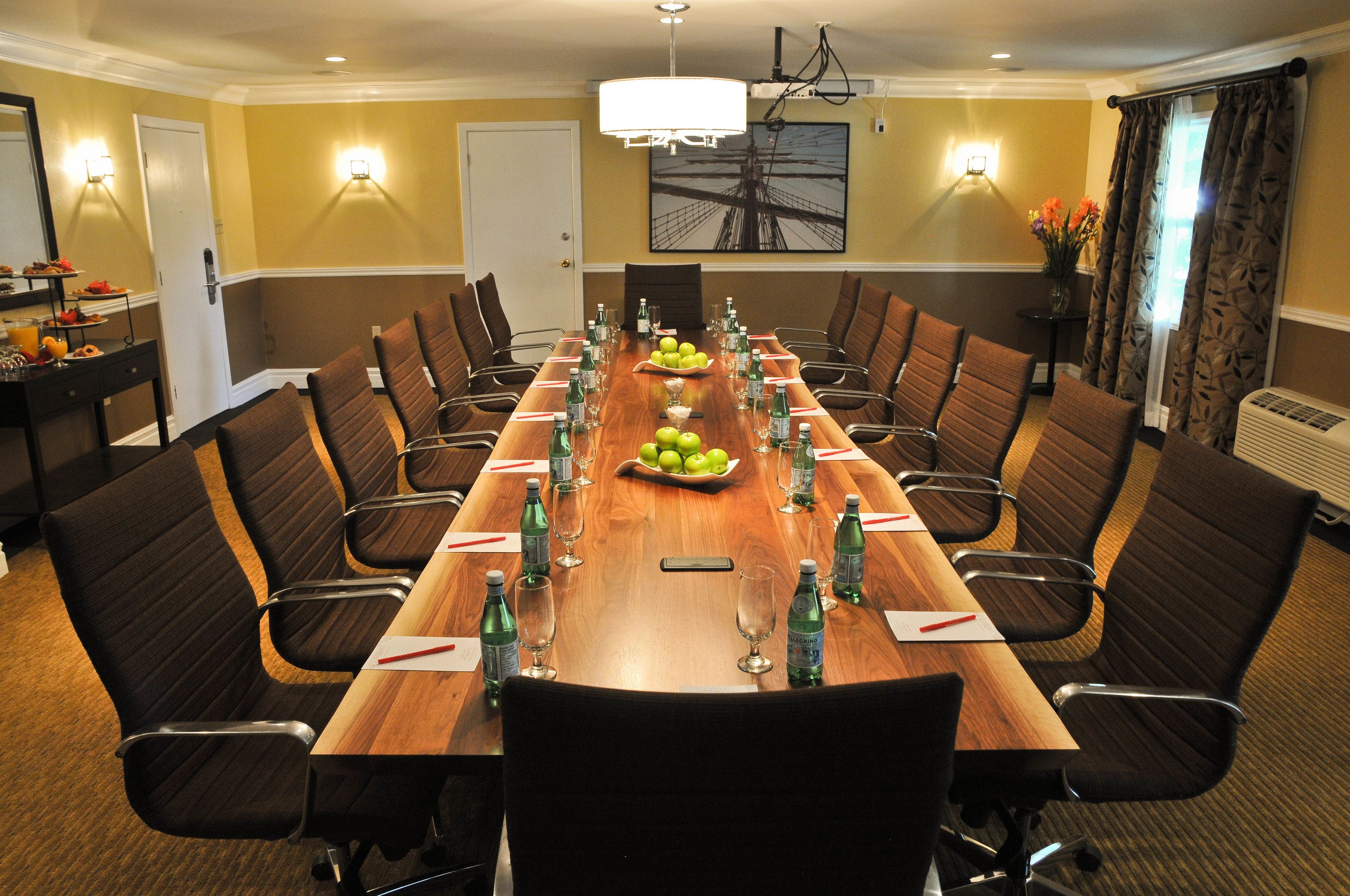 A conference room with a long wooden table, black chairs, and a chandelier.