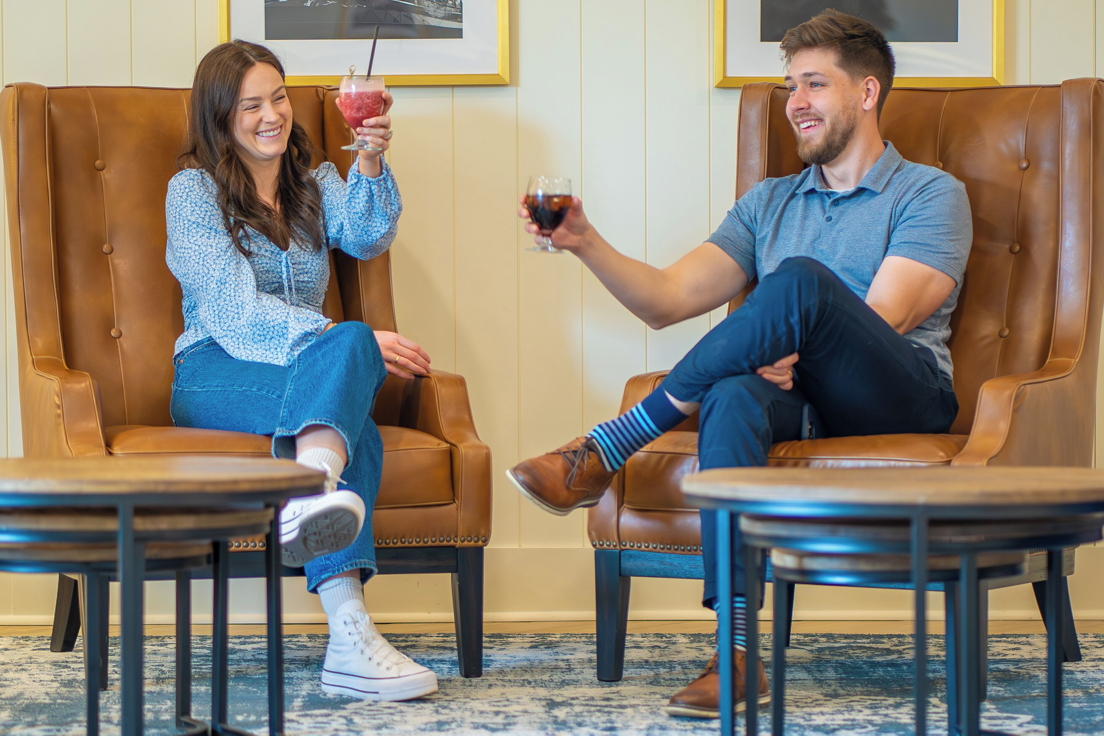 Deux personnes sont assises sur des fauteuils en cuir, face à face, et chacune tient un verre de vin rouge.