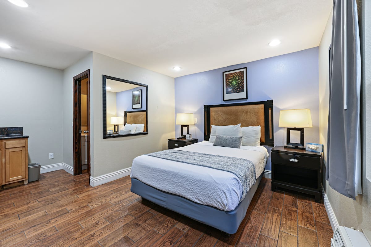 Un dormitorio con una cama grande, dos mesitas de noche con lámparas, un espejo y un cuadro en la pared.