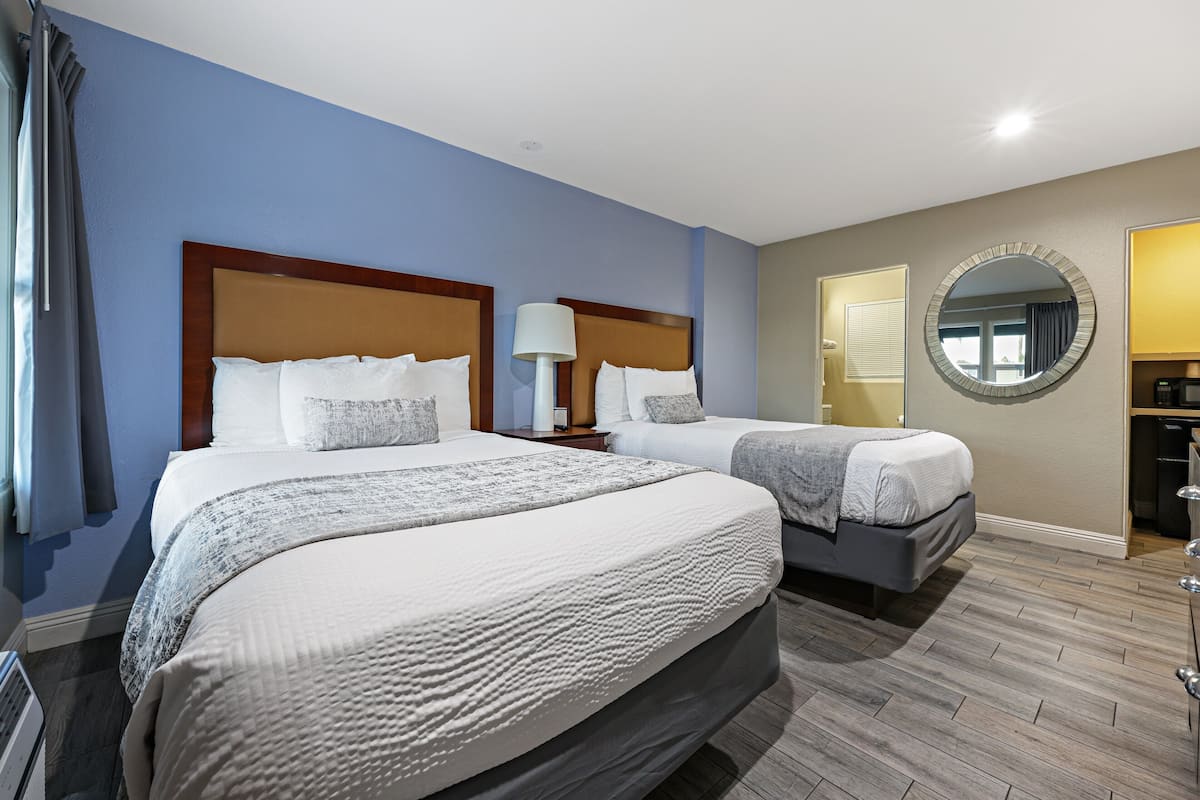 Habitación de hotel con dos camas, un espejo redondo y una pequeña cocina.