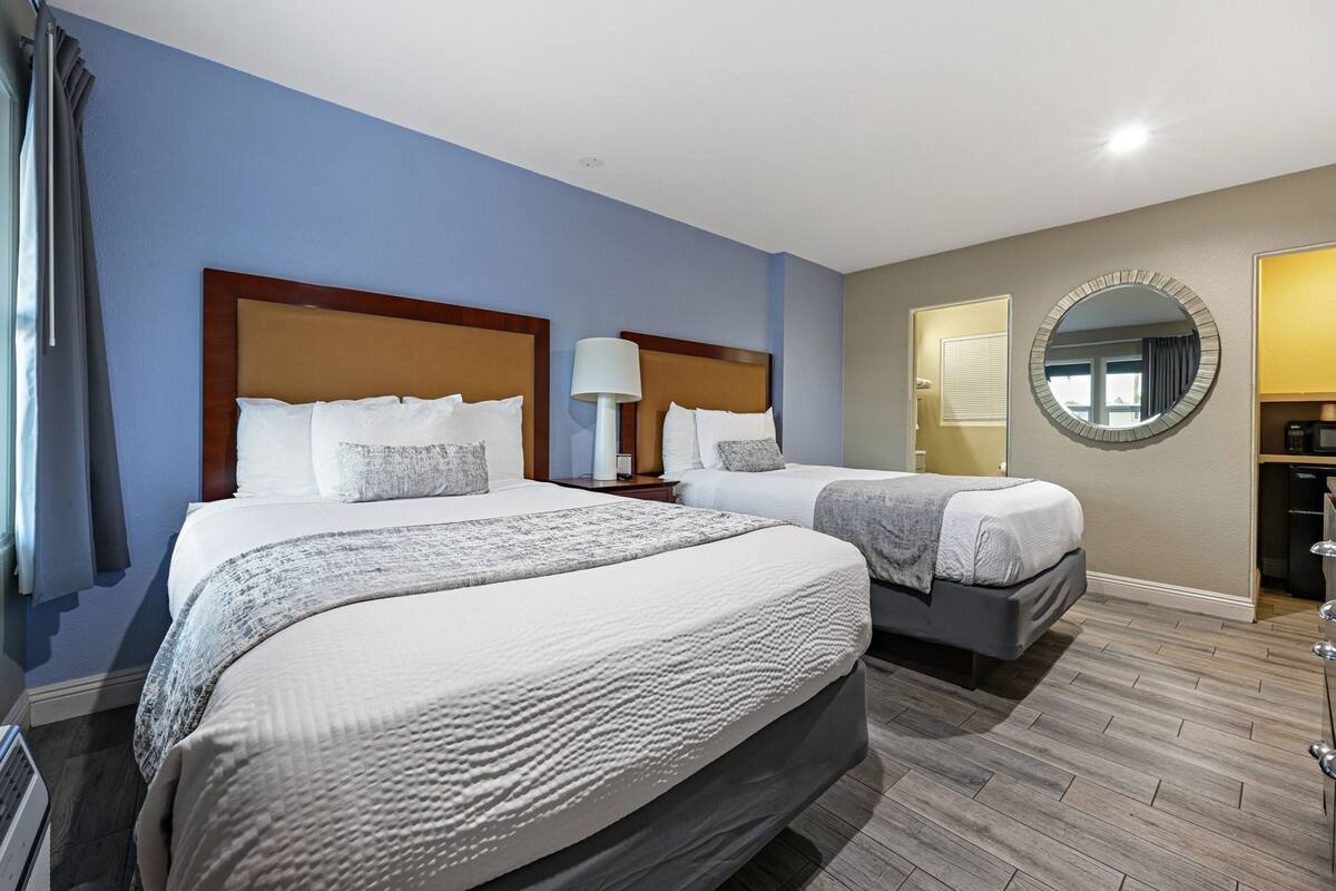 Habitación de hotel con dos camas, un espejo redondo, una mesita de noche con lámpara y un microondas.