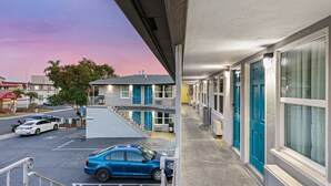 A motel with a covered parking area, a blue car parked in the lot, and a building with blue doors.