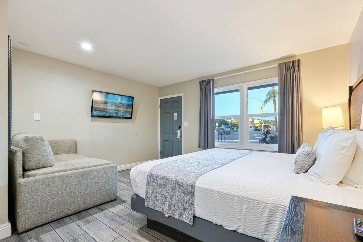 Habitación de hotel con cama, sofá, televisión, ventana y una lámpara.