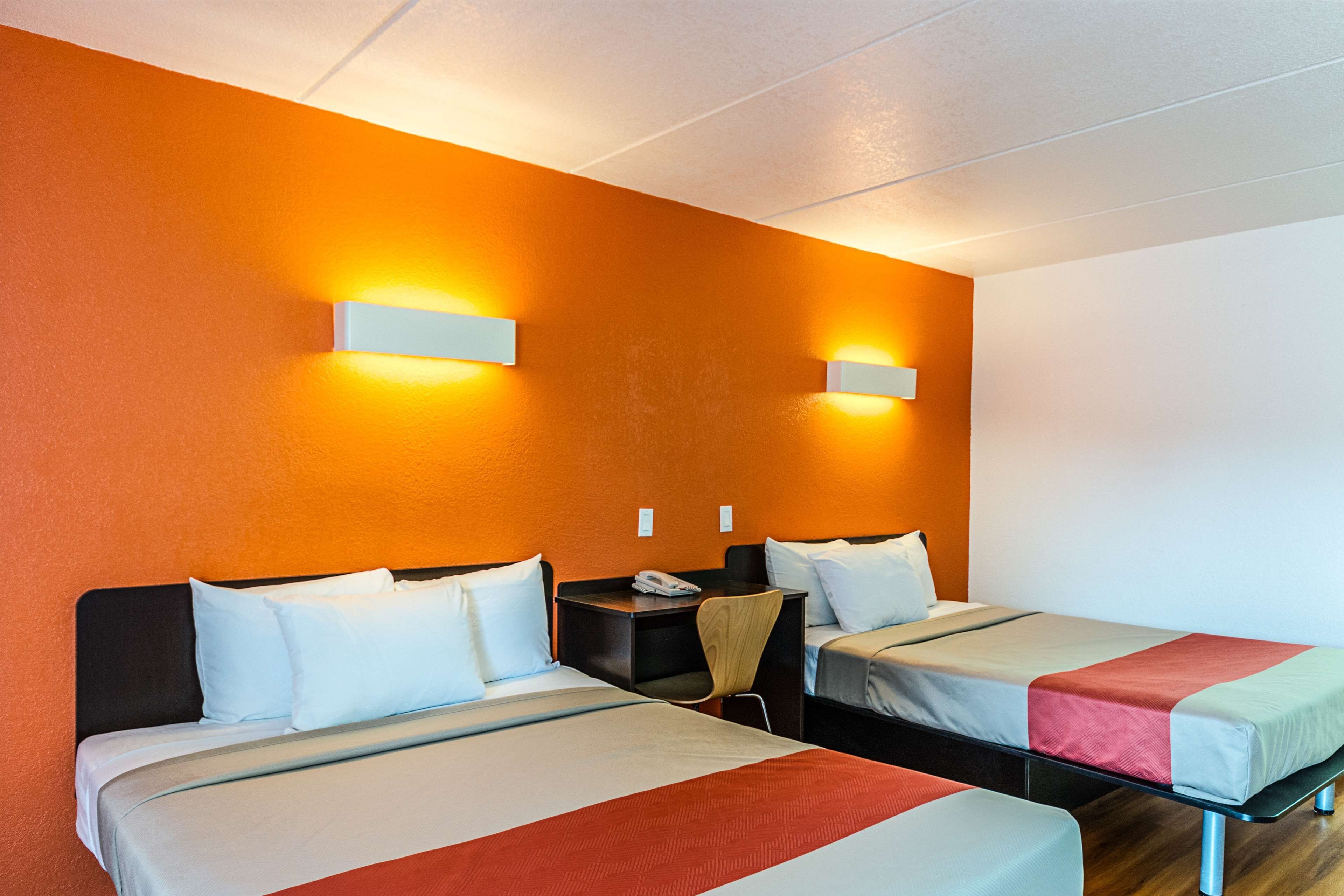 A hotel room with two beds, a desk, and two wall-mounted lights.