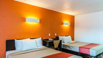 A hotel room with two beds, a desk, and two wall-mounted lights.