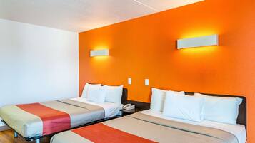 A hotel room with two single beds, each with a bedside table and a lamp. The walls are painted orange, and there are two wall-mounted light fixtures.