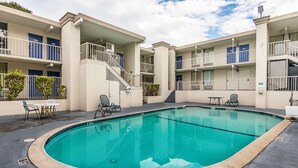 A swimming pool surrounded by a building with multiple balconies and a covered outdoor seating area.