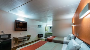 A hotel room with two beds, a desk, a microwave, and a television.