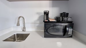 Una cocina compacta con un lavamanos de acero inoxidable, un microondas y una cafetera.