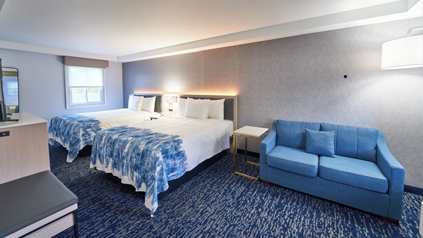 A hotel room with a large bed, a blue sofa, a desk, and a window. - The Bridgeway (Buzzards Bay)